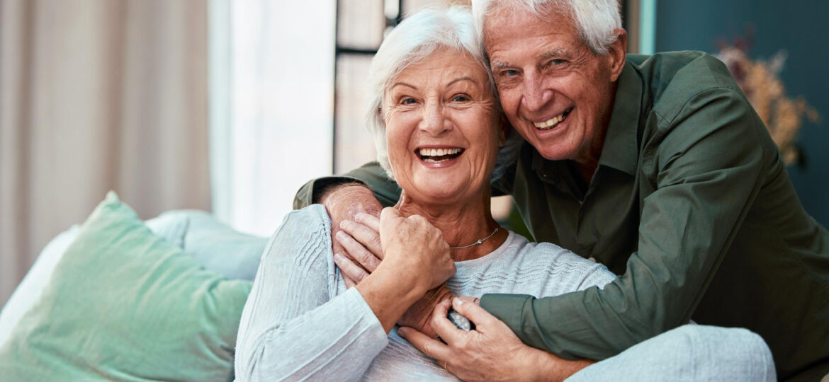 portrait-hug-senior-couple-living-room-home-smiling-bonding-love-retirement-smile-happy-elderly-man-woman-sofa-embrace-enjoying-quality-time-together-house