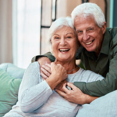 portrait-hug-senior-couple-living-room-home-smiling-bonding-love-retirement-smile-happy-elderly-man-woman-sofa-embrace-enjoying-quality-time-together-house