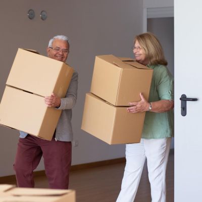 smiling-elderly-couple-moving-into-new-house-retired-husband-wife-holding-cardboard-boxes-downsizing