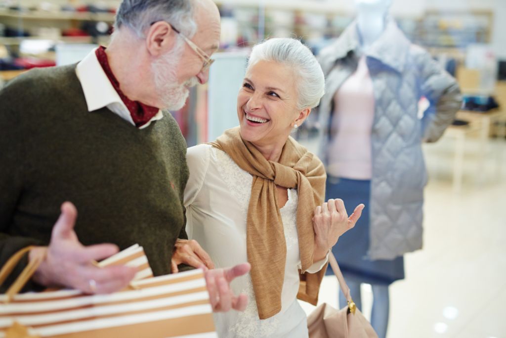 Smiling senior couple shopping together in a lively retail area, highlighting the benefits of a well-located senior living community with easy access to amenities.