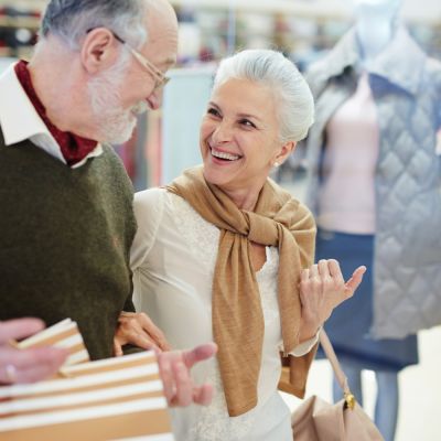 Smiling senior couple shopping together in a lively retail area, highlighting the benefits of a well-located senior living community with easy access to amenities.